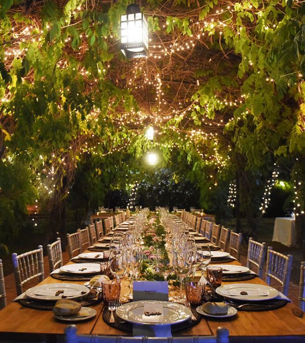 Elegante mesa imperial al aire libre decorada con guirnaldas de luces entre ramas, ambientación nocturna de Antonio Bort en Espartinas, Sevilla.
